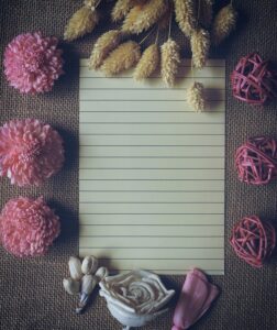 Flat lay of a lined paper surrounded by pink flowers and rustic elements on jute fabric.