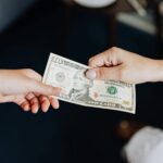 Two people exchanging a ten dollar bill in a close-up hand-to-hand transaction.
